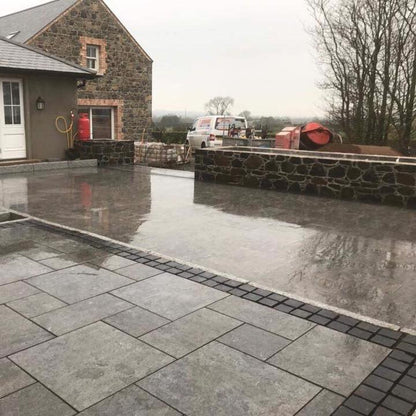 Paved patio area in front of a stone building with a cloudy sky. Patio edging is Black Limestone Paving Cobbles in 100 x 100mm