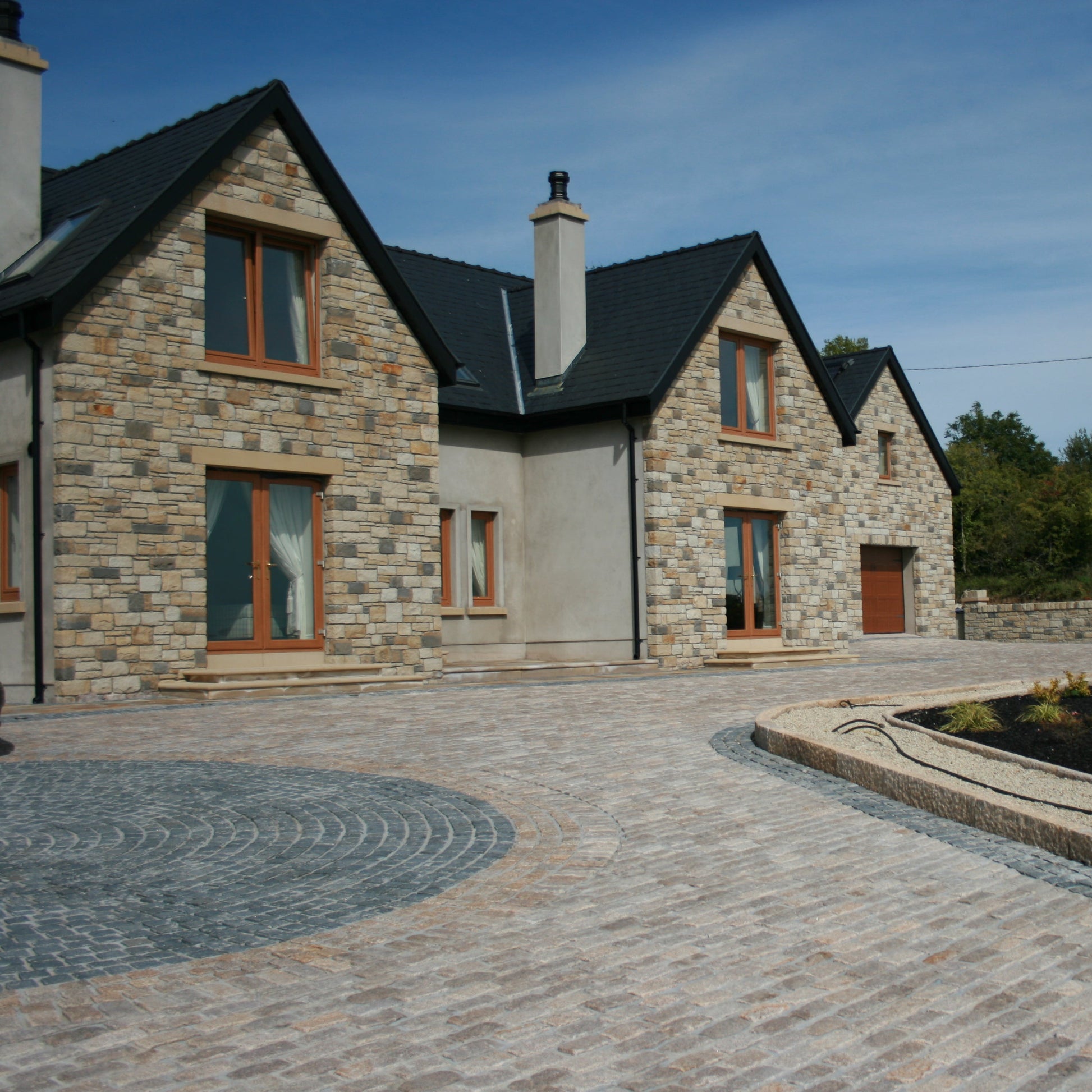Stone house with a driveway leading up to it, surrounded by greenery. Driveway design features Black Limestone Cobbles in 100 x 100mm size. 