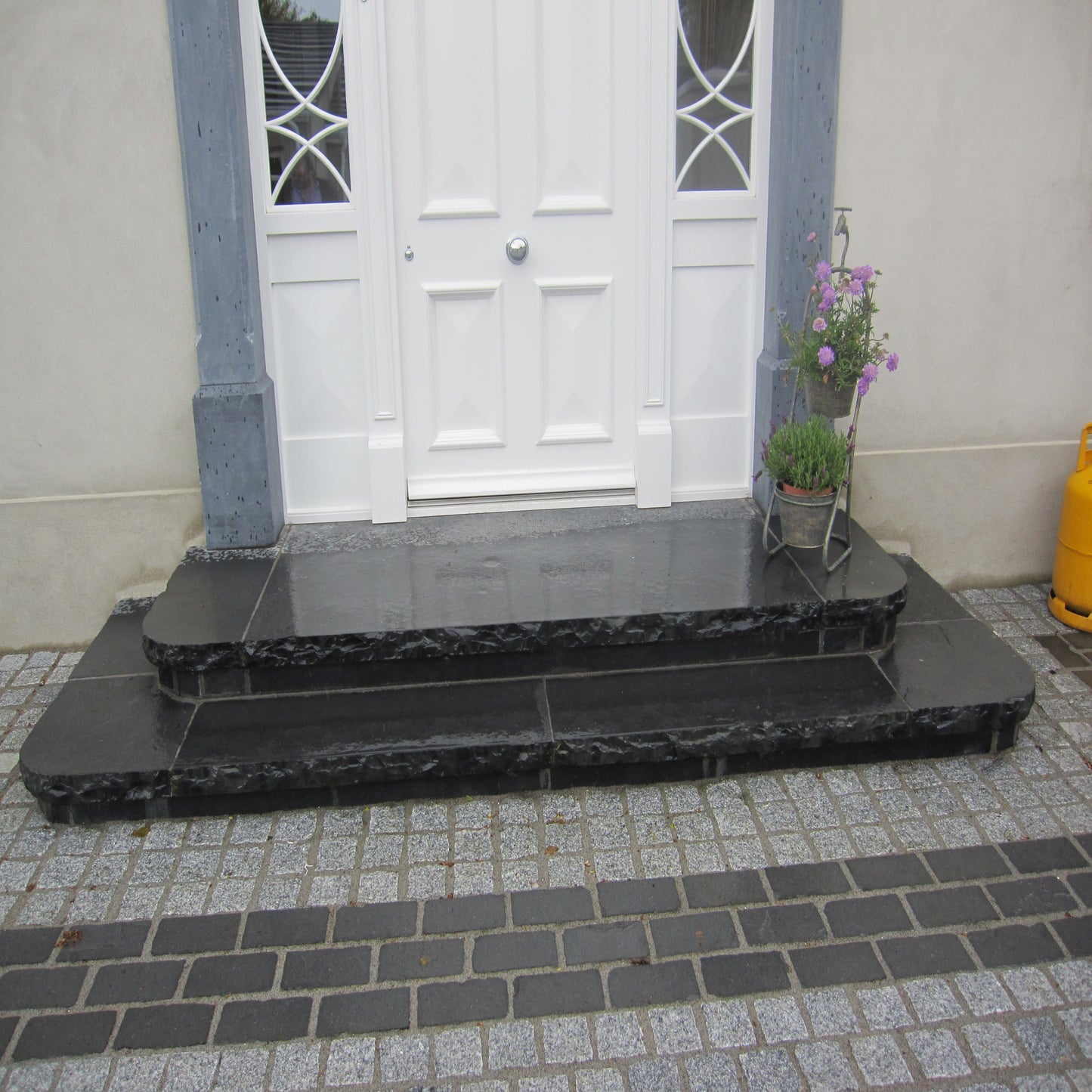 Black limestone cobbles installed on a front doorstep area, with a white door and a potted plant to the side.