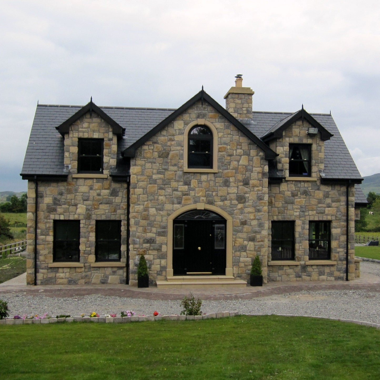 Stone house with a driveway and green landscape. Stone is Blue Centre Sandstone Machined and Architectural Sandstone Surrounds, Sills and Steps. 