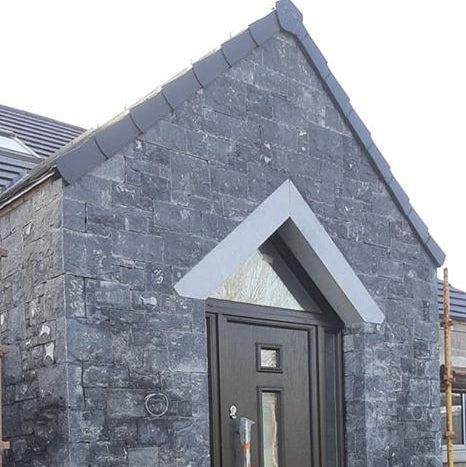 Modern house entrance with a dark door and stone façade featuring an angled blue limestone door lintel with a sanded finish. 