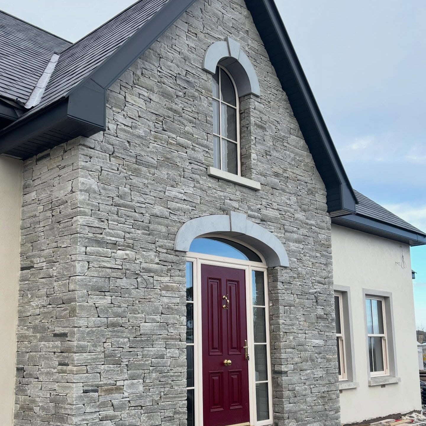 House exterior with stone façade and red door. House features bespoke blue limestone arched lintels with keystone. 
