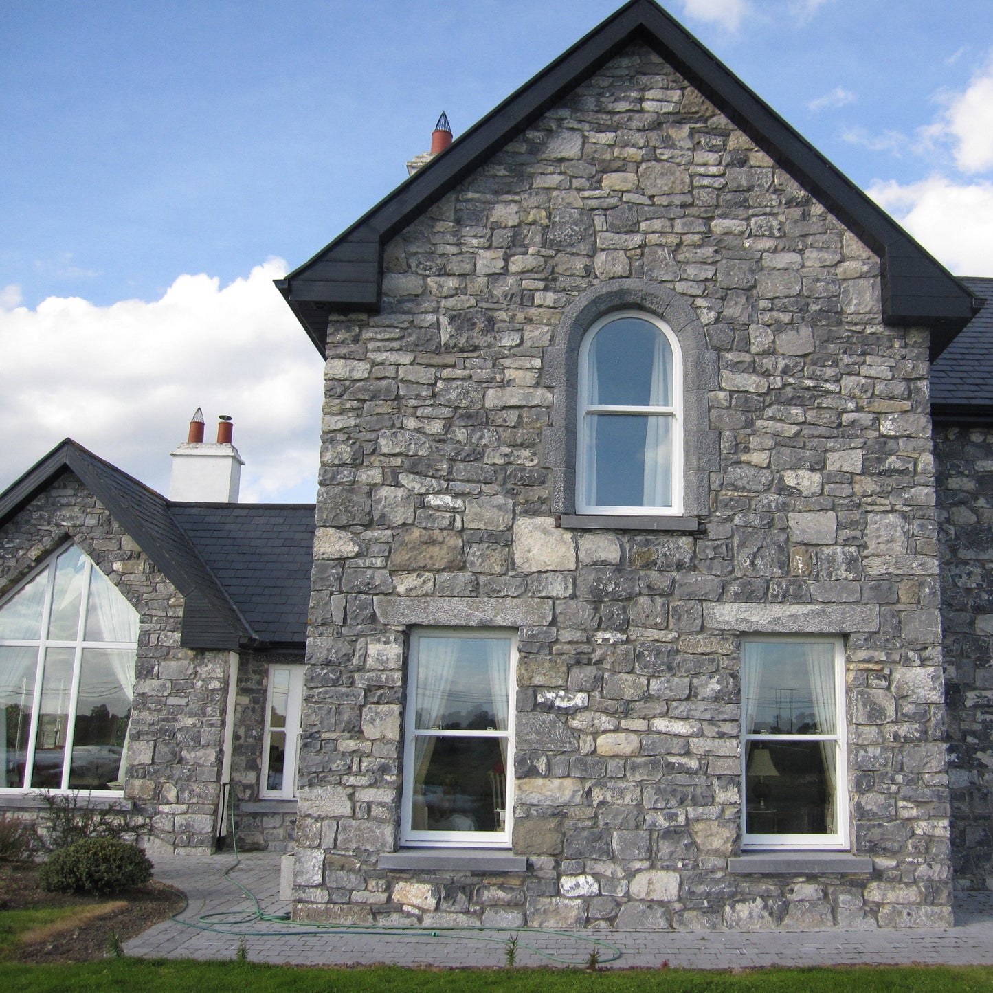 Stone house with black roof against a blue sky. Windows feature bespoke blue limestone window lintels. 