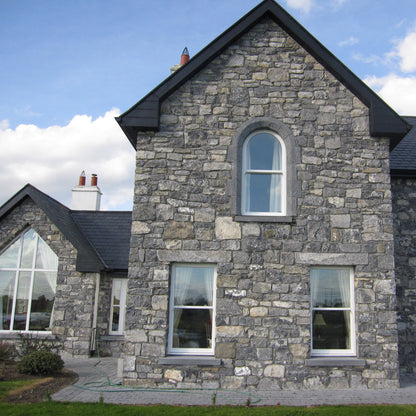 Stone house with black roof against a blue sky. Windows feature bespoke blue limestone window lintels. 