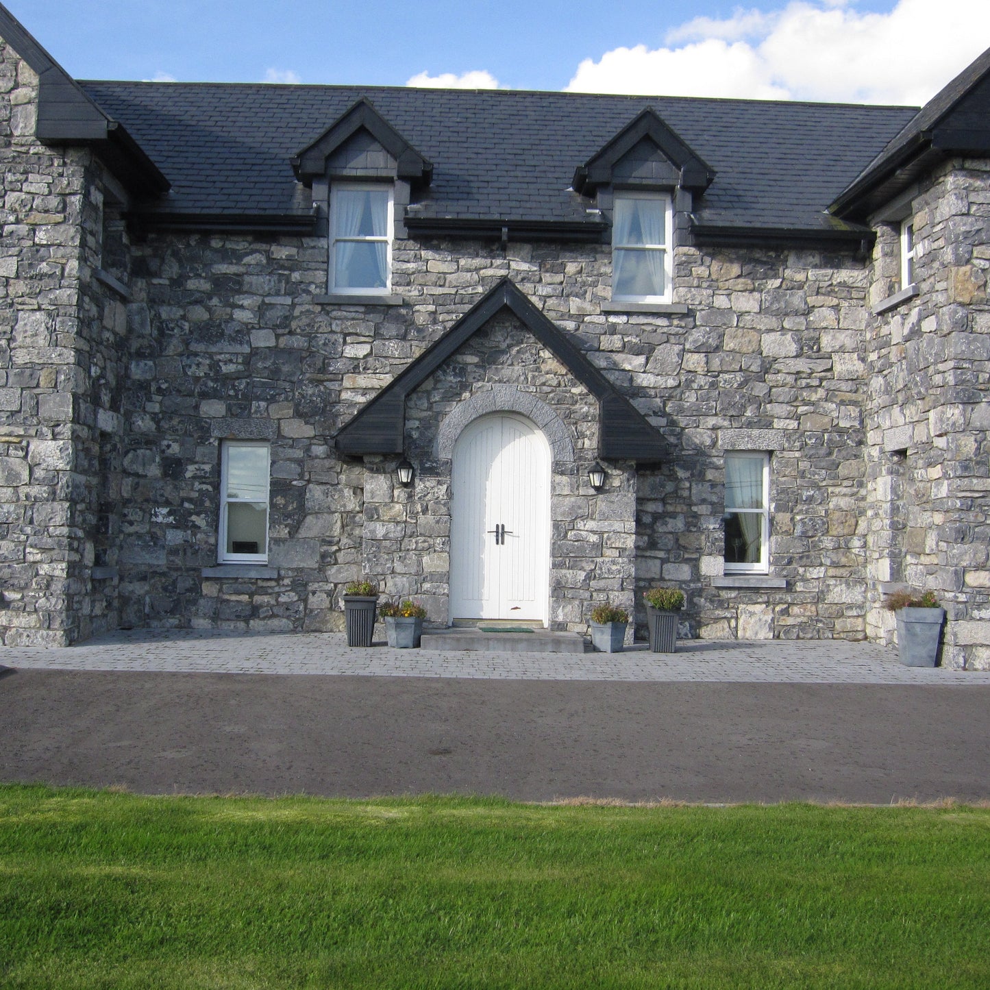 Stone house with a white door and black roof, surrounded by green grass. Window and door features bespoke blue limestone lintels