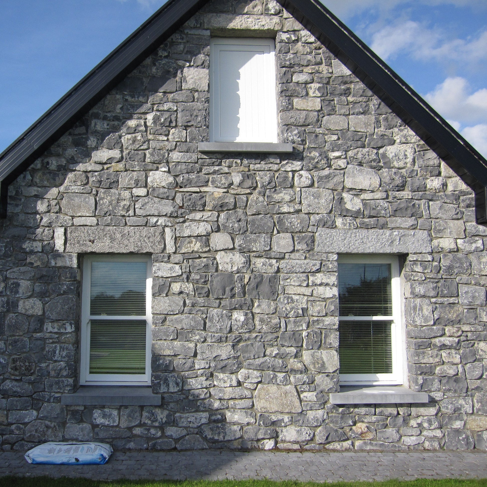 Stone house with a blue sky and clouds in the background. Stone façade features bespoke blue limestone lintels with a punched finish.
