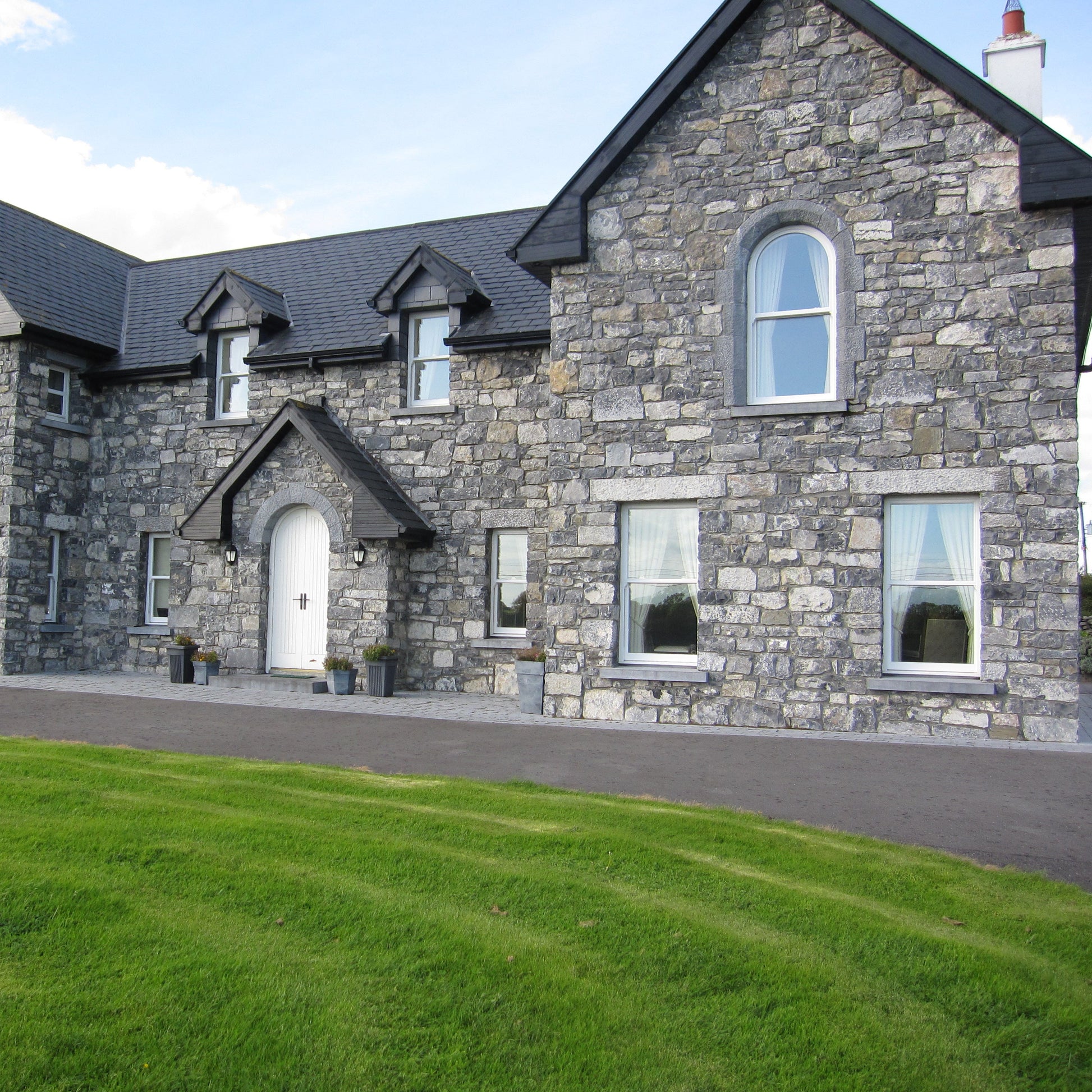 Large stone house with a well-maintained lawn and driveway. House features bespoke Blue Limestone Lintels and Sills with a punched finish.