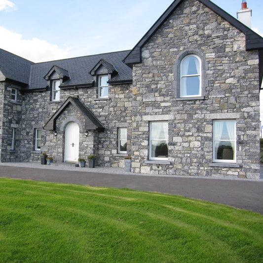 Large stone house with a well-maintained lawn and driveway. House features bespoke Blue Limestone Lintels and Sills with a punched finish.