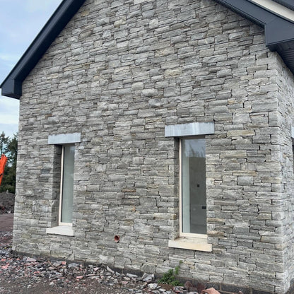 House with stone façade and two windows with bespoke blue limestone lintels on a clear day.