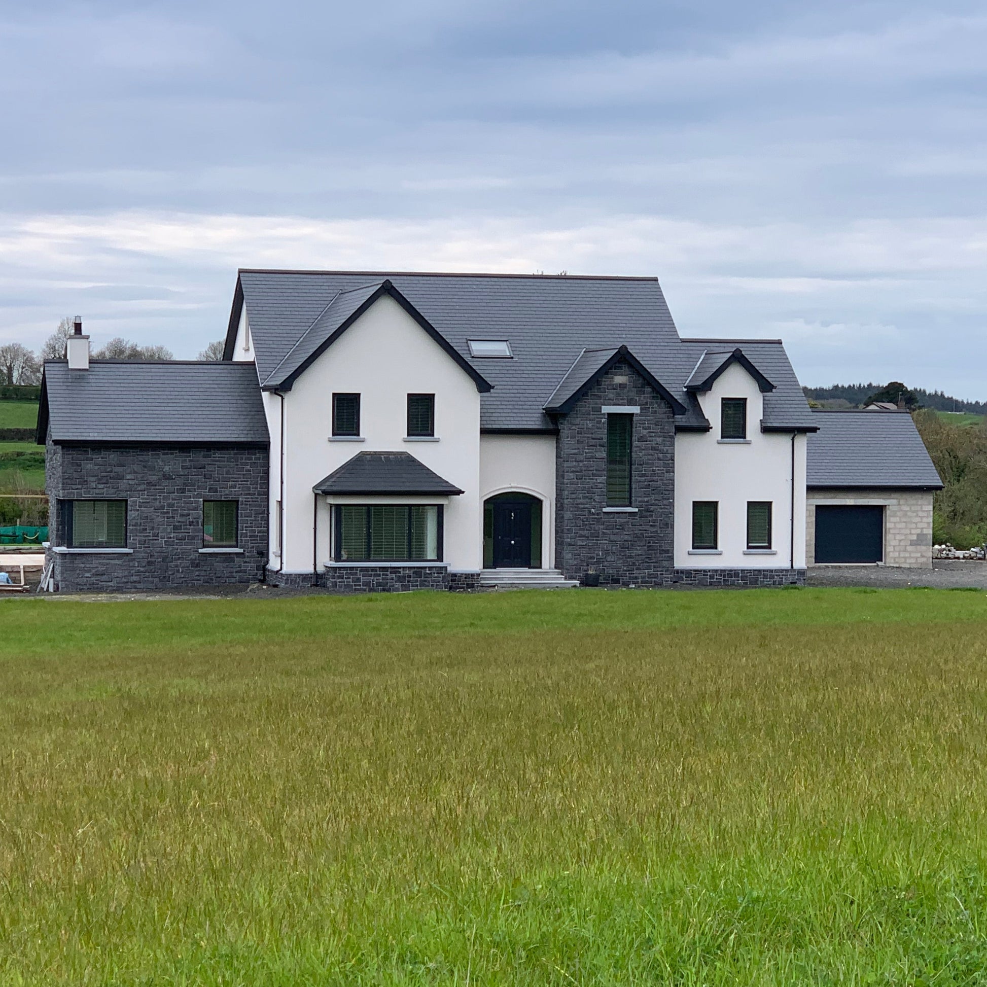 Large modern house with blue limestone machined walling stone feature facades and black roof in a rural setting.