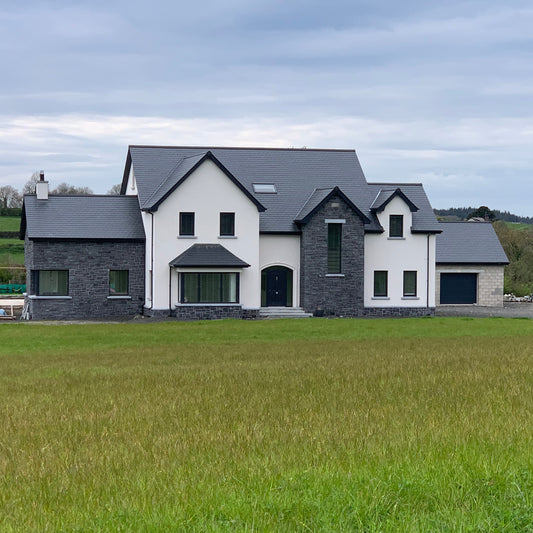 Large modern house with blue limestone machined walling stone feature facades and black roof in a rural setting.
