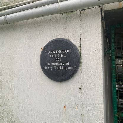 Plaque commemorating Turkington Tunnel with year 1991 and name Harry Turkington on a white wall.