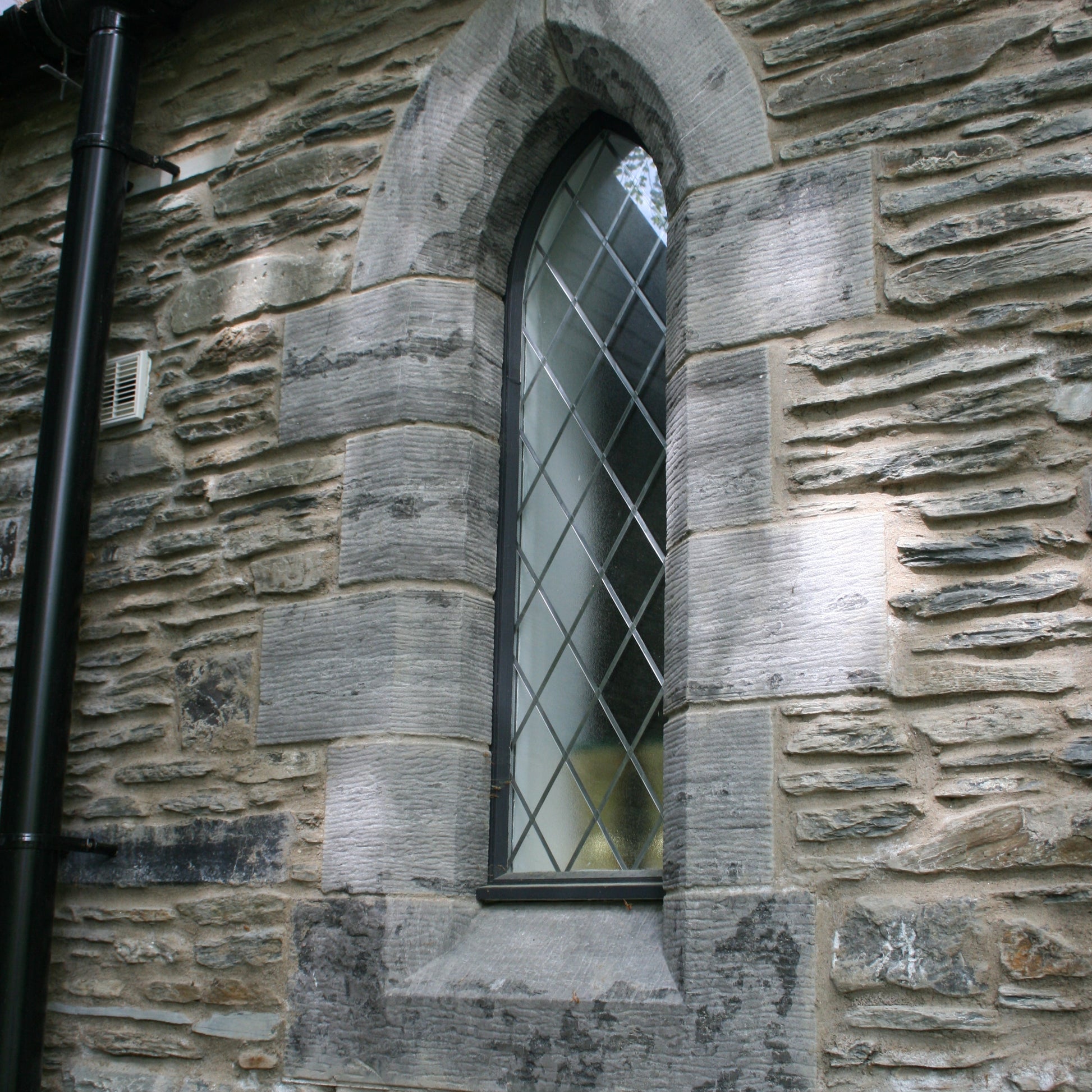 Stone wall with a window featuring diamond-patterned glass and bespoke limestone quoins. 