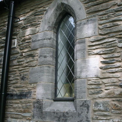 Stone wall with a window featuring diamond-patterned glass and bespoke limestone quoins. 