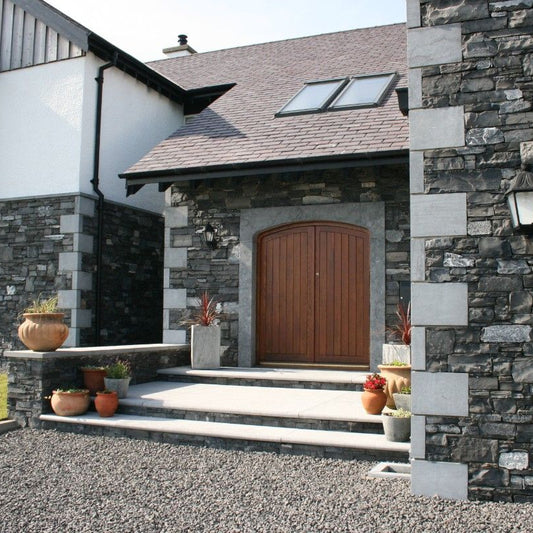 A building entrance featuring architectural Limestone door surround and quoins on the corners of the structure, with a stone wall and a wooden door.