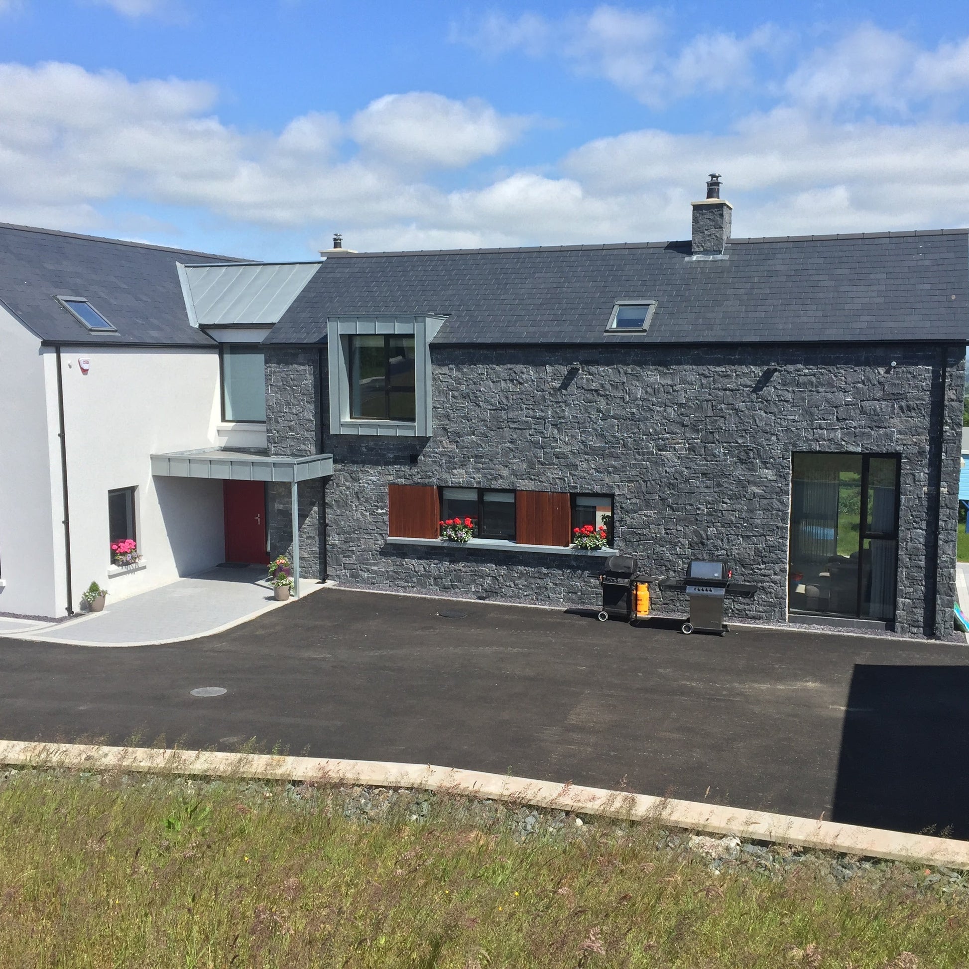 Modern new build partially cladded in Blue Limestone Stoneer Cladding with tarmac street.