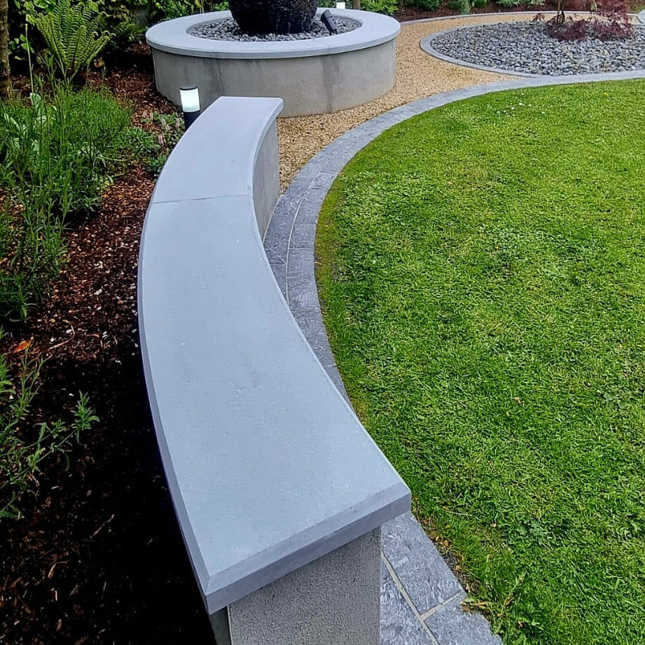 Garden scene with a curved stone bench completed with bespoke blue limestone wall capping, garden features, and trees.