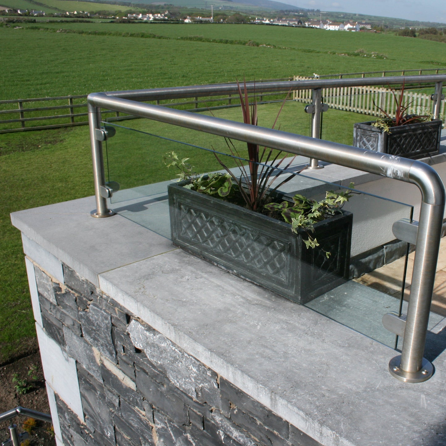 Terrace with glass panels and metal railings on top of bespoke blue limestone wall capping overlooking a green landscape