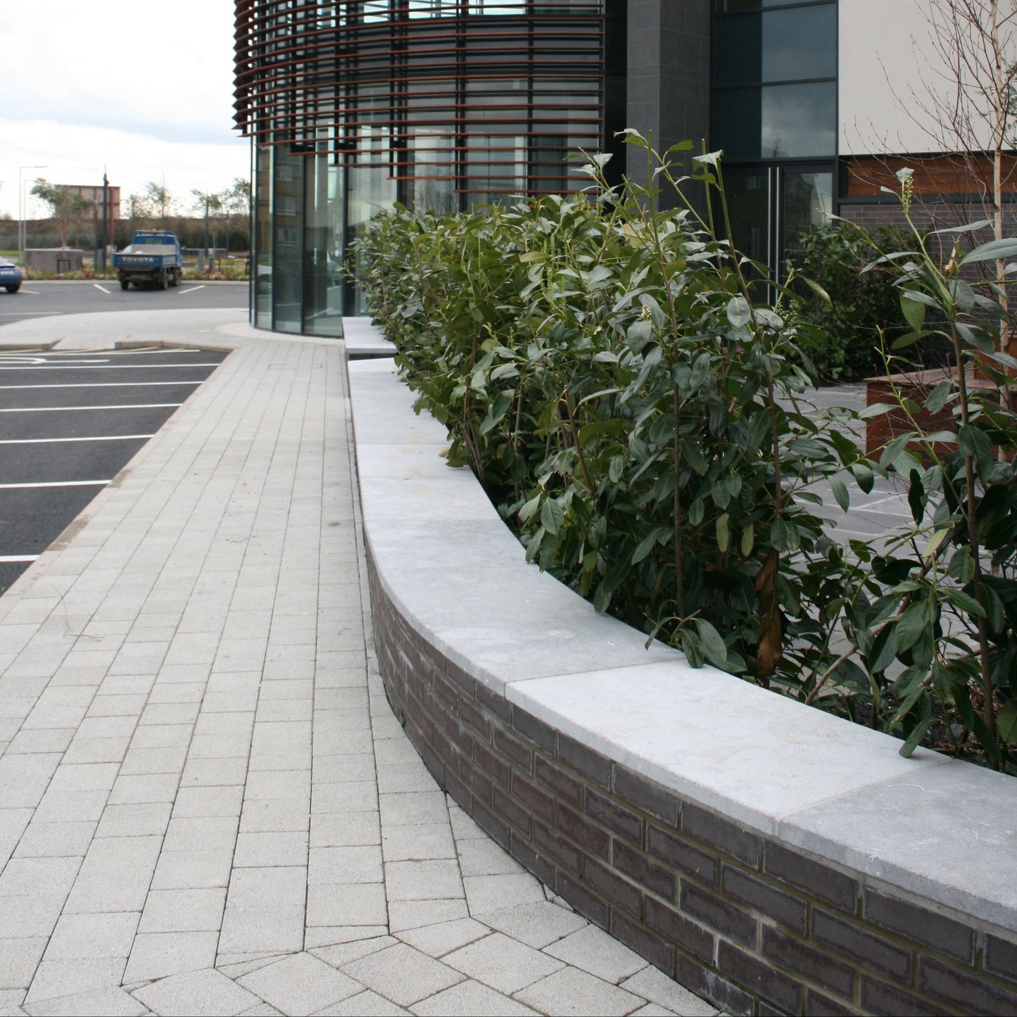 Curved bespoke blue limestone wall capping on a low brick wall along a pathway towards a commercial building. 