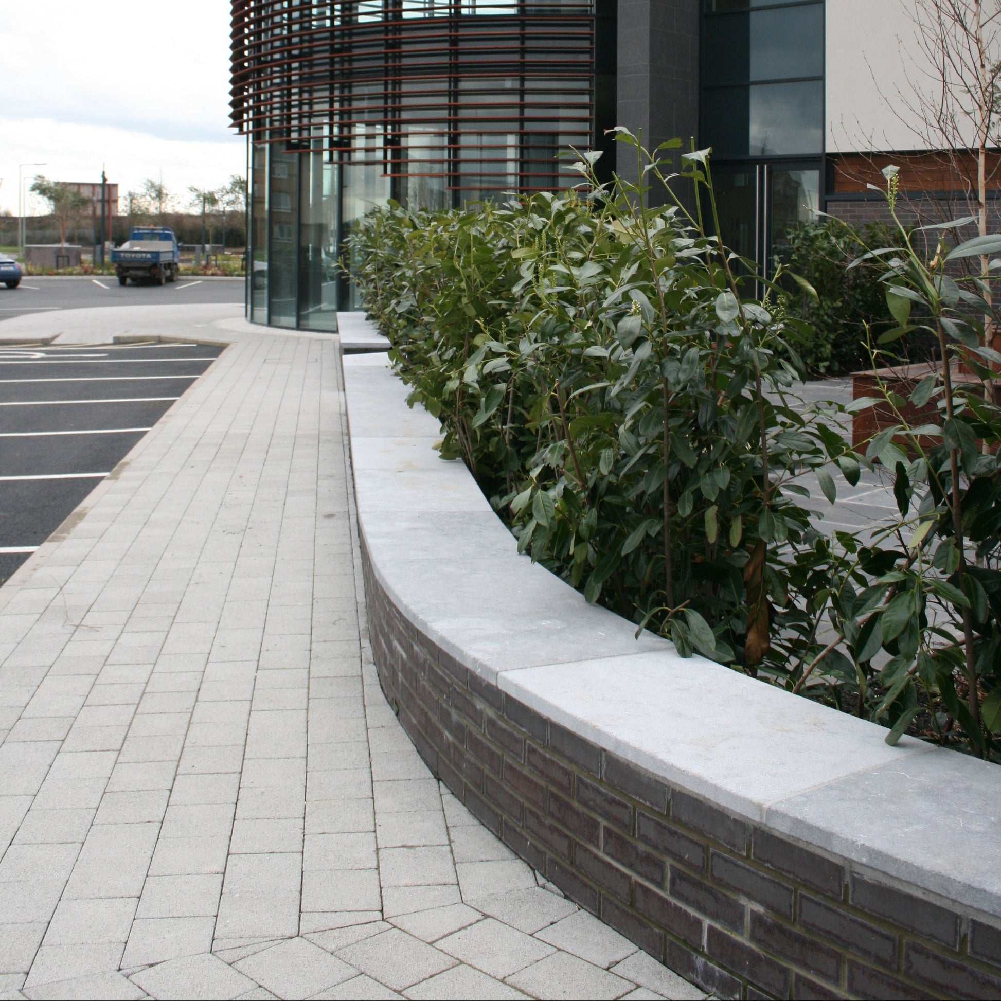 Curved bespoke blue limestone wall capping on a low brick wall along a pathway towards a commercial building. 