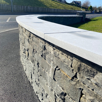 Bespoke flat blue limestone wall capping along a curved stone boundary wall.