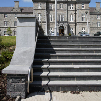 Stone wall alongside steps leading up to a pavement. Wall completed with bespoke blue limestone wall capping. 