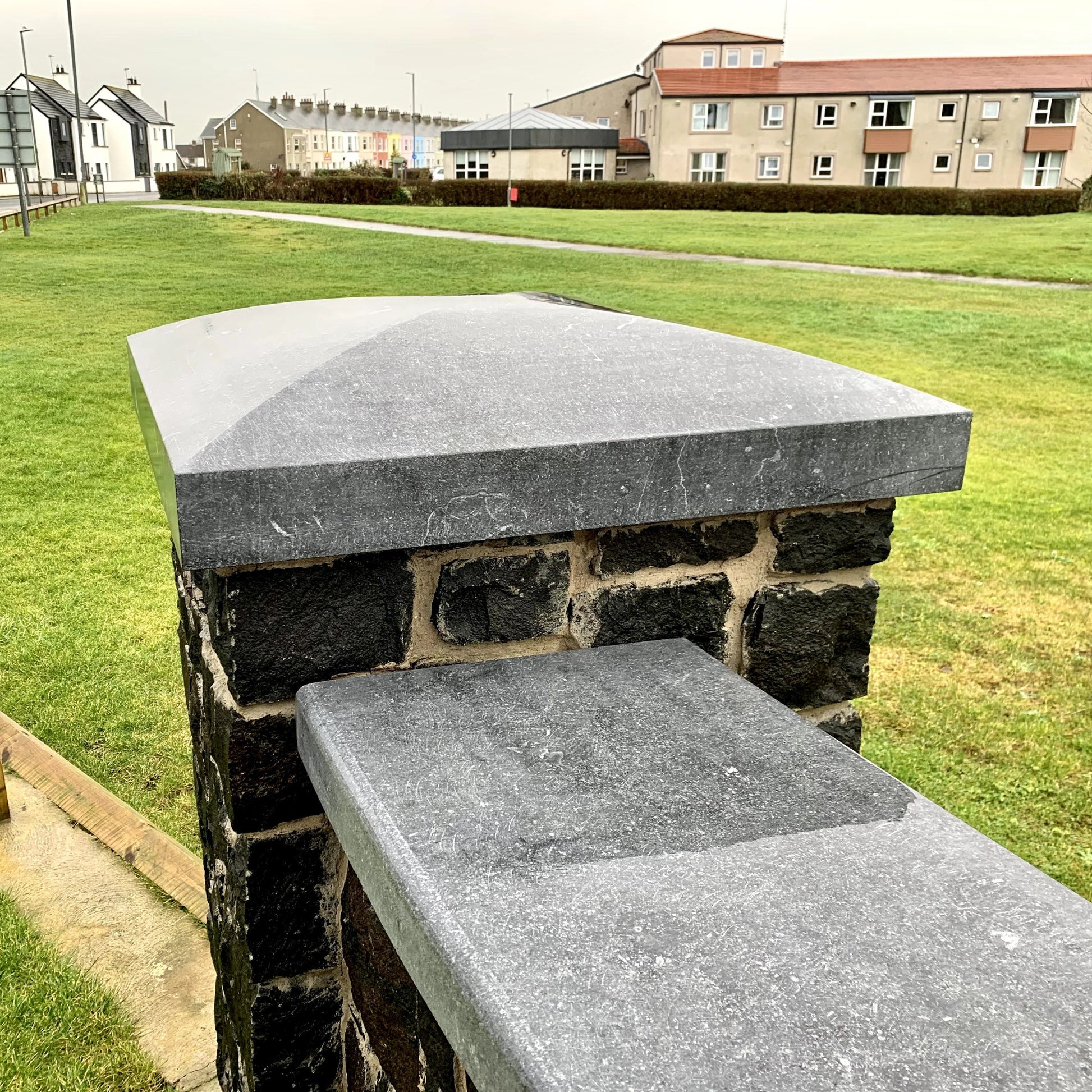 Bespoke blue limestone pillar cap and wall capping with houses and grass in the background. 