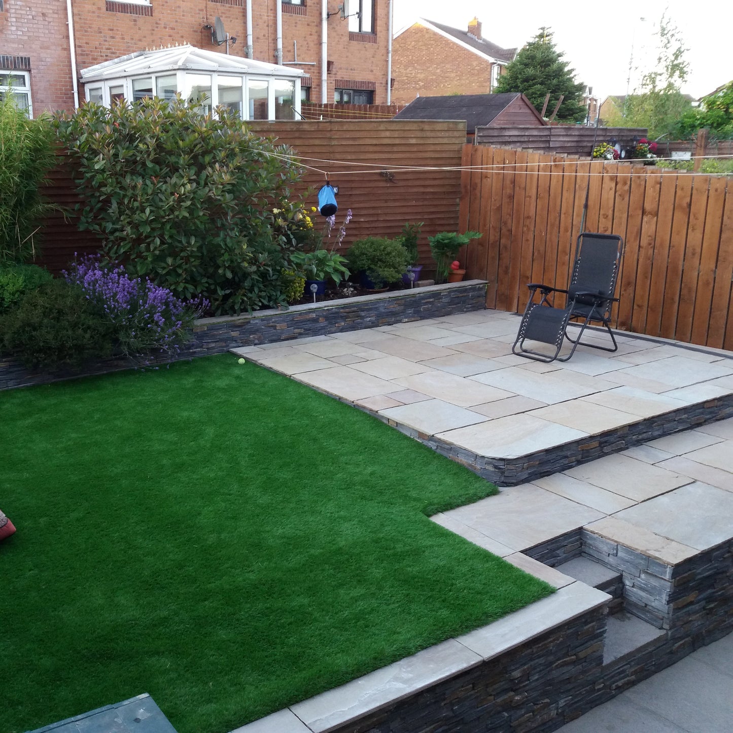 Small patio on raised garden featuring Camel Dust Sandstone Paving photographed dry. 