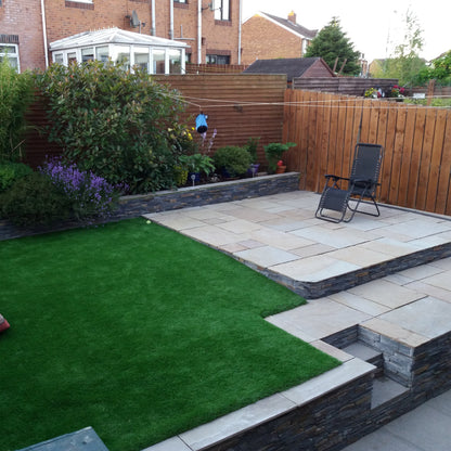 Small patio on raised garden featuring Camel Dust Sandstone Paving photographed dry. 