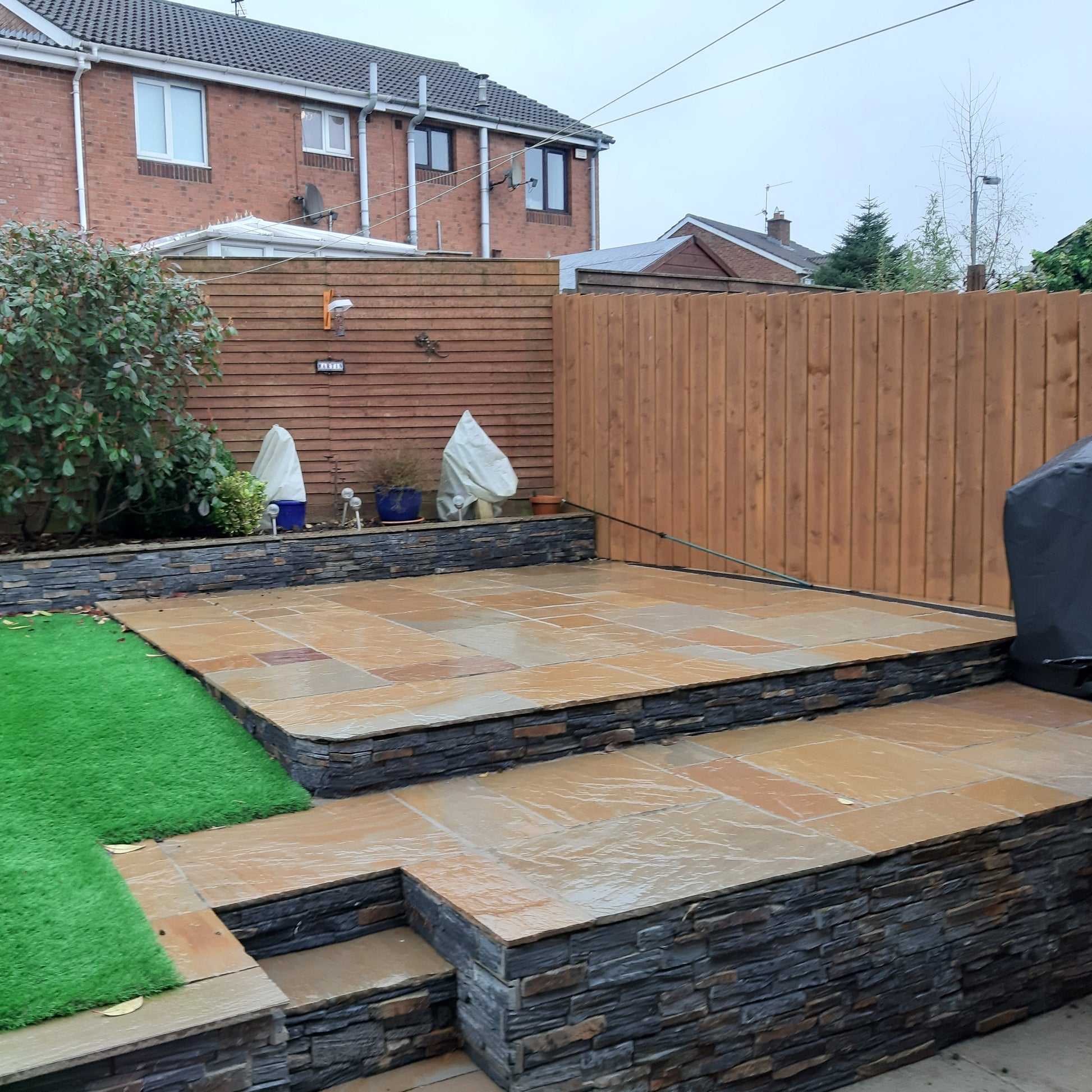 Small patio area on raised garden featuring Camel Dust Sandstone Paving. Photographed wet. 