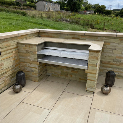 BBQ and stone wall in a paved patio area. Paving is Camel Jewel Range Porcelain Paving. 