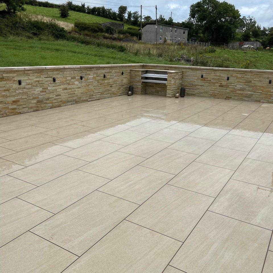 Large patio area featuring Camel Jewel Range Porcelain Paving Tiles in 900 x 600 x 20mm size. BBQ and Stone wall in the background.  