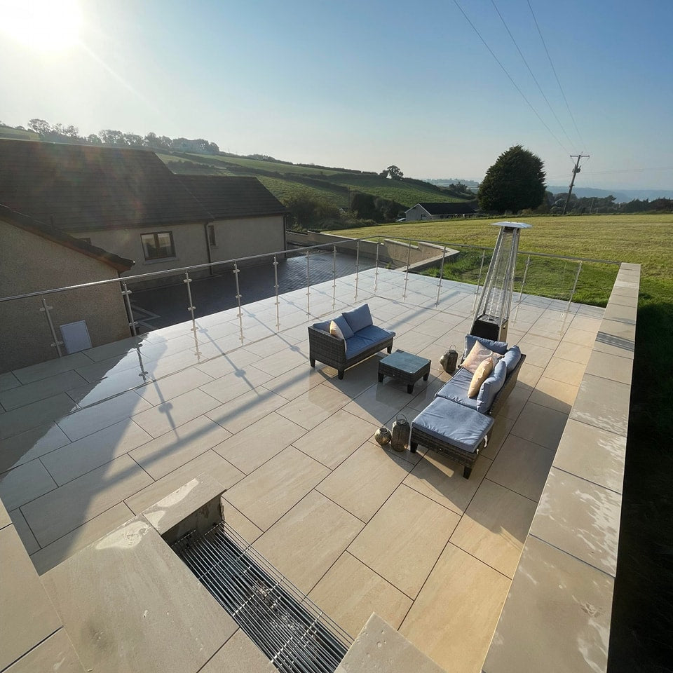 Large raised patio with BBQ and garden furniture overlooking a field and house. Patio completed using Camel Jewel Range Porcelain Paving. 