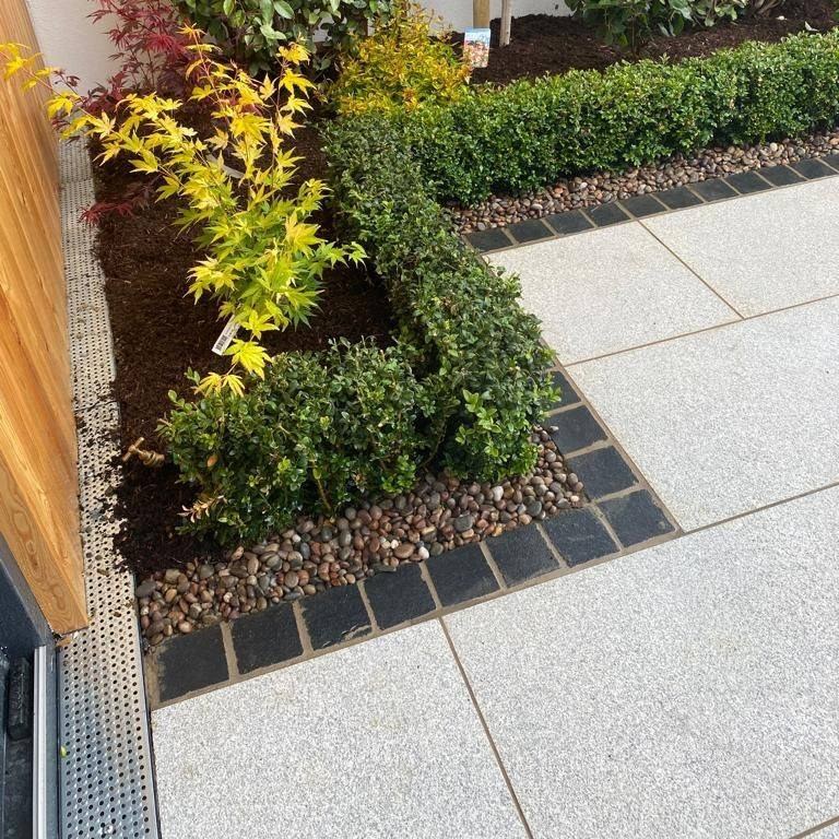 Close up of Camel Jewel Range Porcelain Tiles with a black cobble border surrounded by planting. 