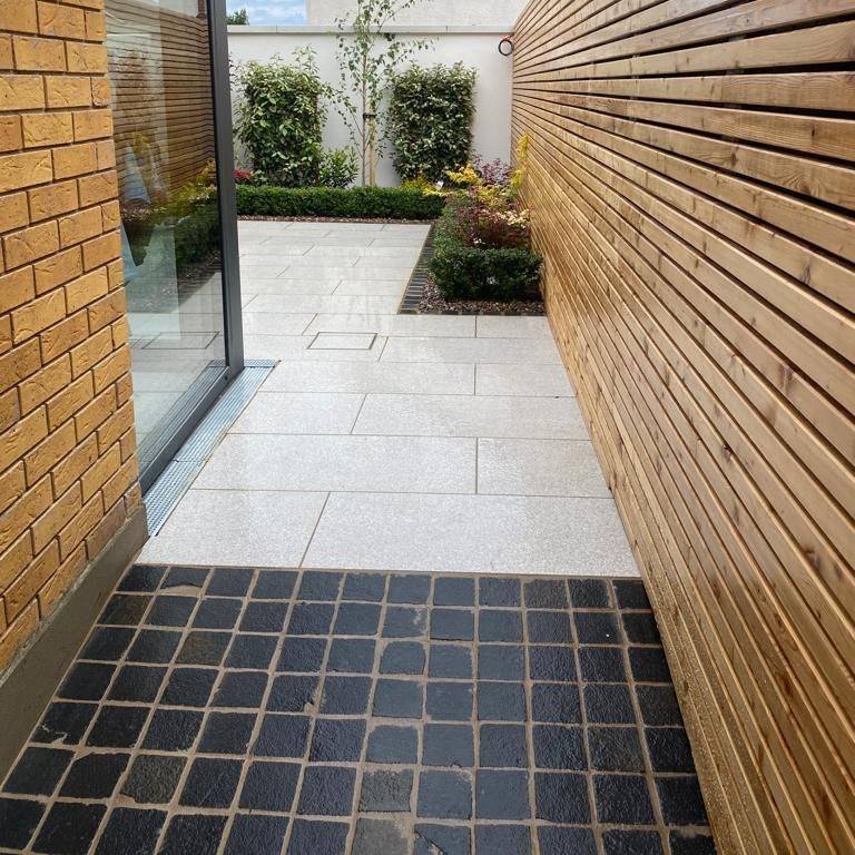 View of patio area, planting and modern fencing. Paving is Camel Jewel Range Porcelain Paving with black cobbles. 