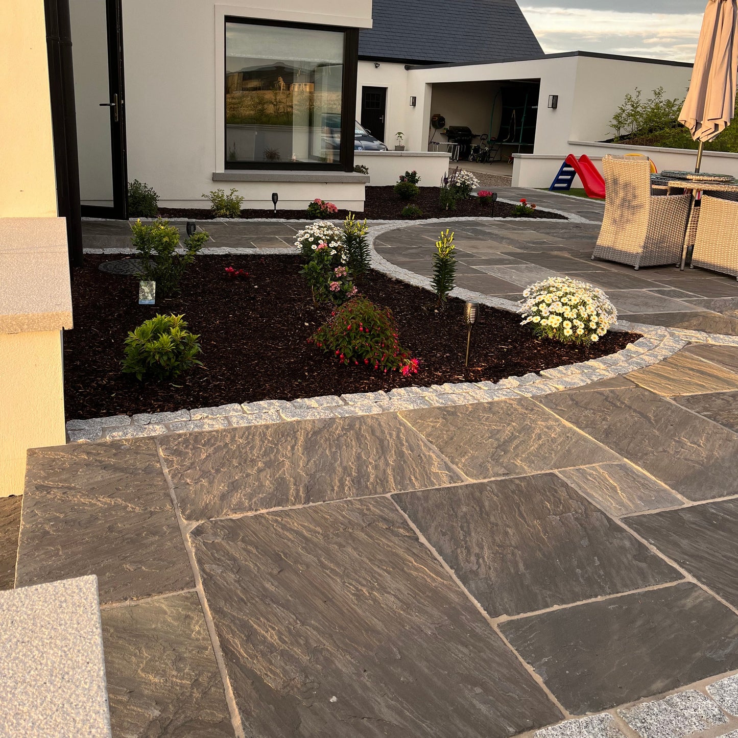 Modern house exterior with a stone pathway in Cider Black Sandstone and garden.