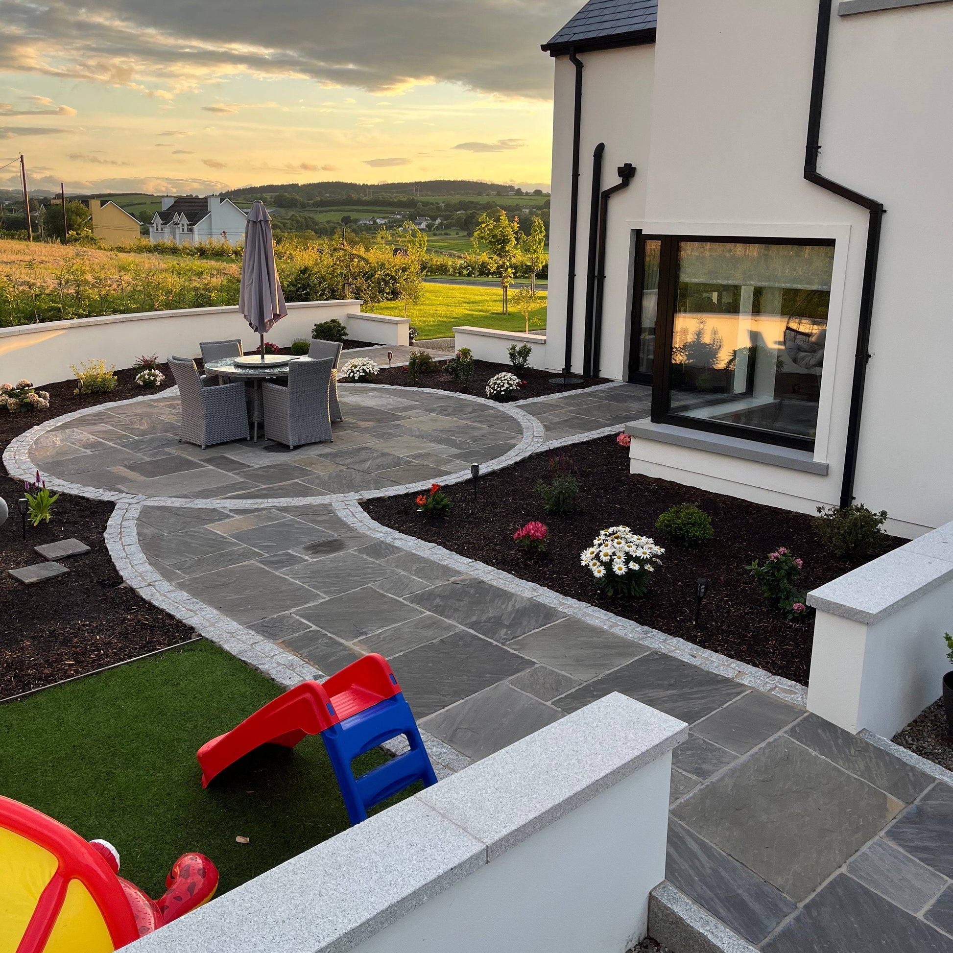 Modern house exterior with a patio area in Cider Black Sandstone Paving and garden.