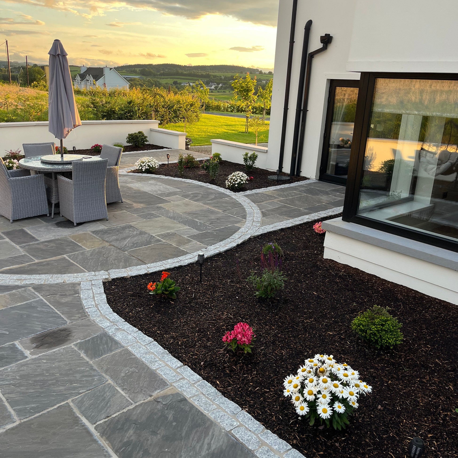 Patio area with a garden and sunset view. Paving is Cider Black Sandstone Patio Packs. 