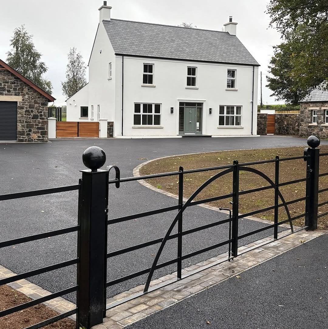 White house with a grey roof and black gate in a residential area. Cobble detail at gate entrance featuring Cider Black Sandstone Paving Setts. 