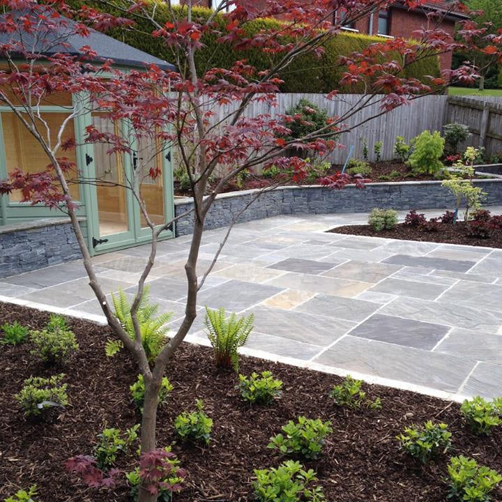 Patio area with outside room surrounded by planting and low level stone wall. Patio paving completed using Cider Black Sandstone Patio Packs. 