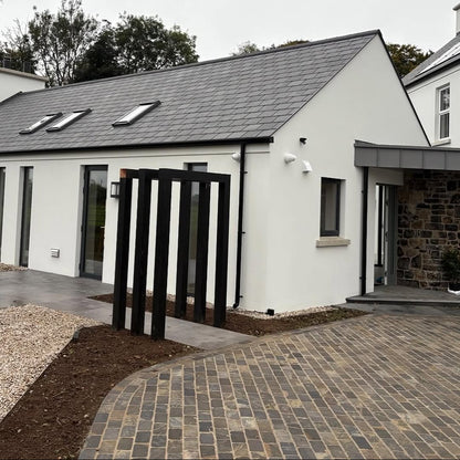 Modern house exterior with white walls, grey roof, and black metal garden feature. Paving features Cider Black Sandstone Paving Setts.