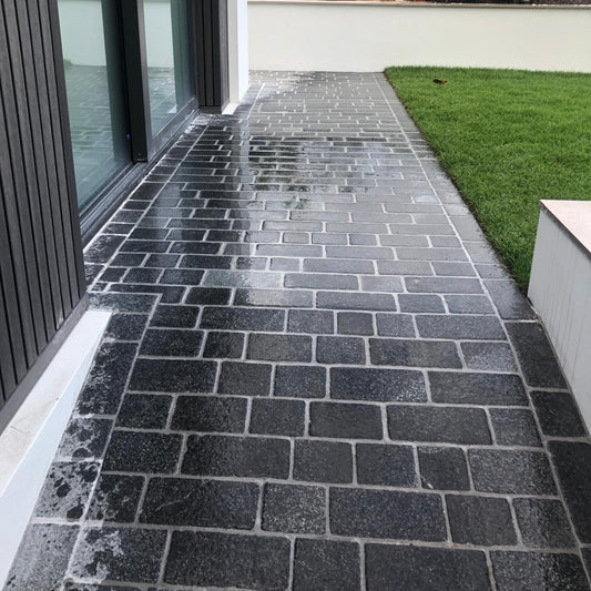 A pathway photographed wet laid out with Coachman's  Black Granite Paving Setts, showing a contemporary look with a flamed surface finish and tumbled edges.