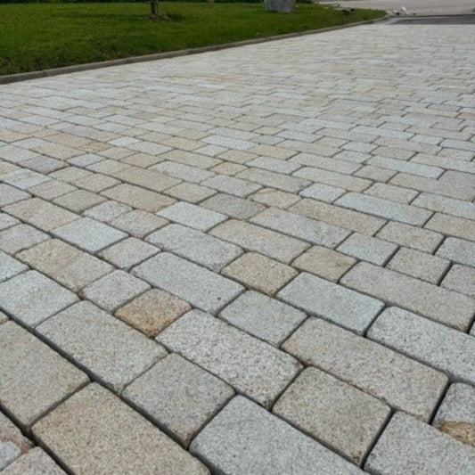 A close-up view of Coachman's Gold Granite Paving Setts arranged on a surface, displaying their golden hue and natural split texture.