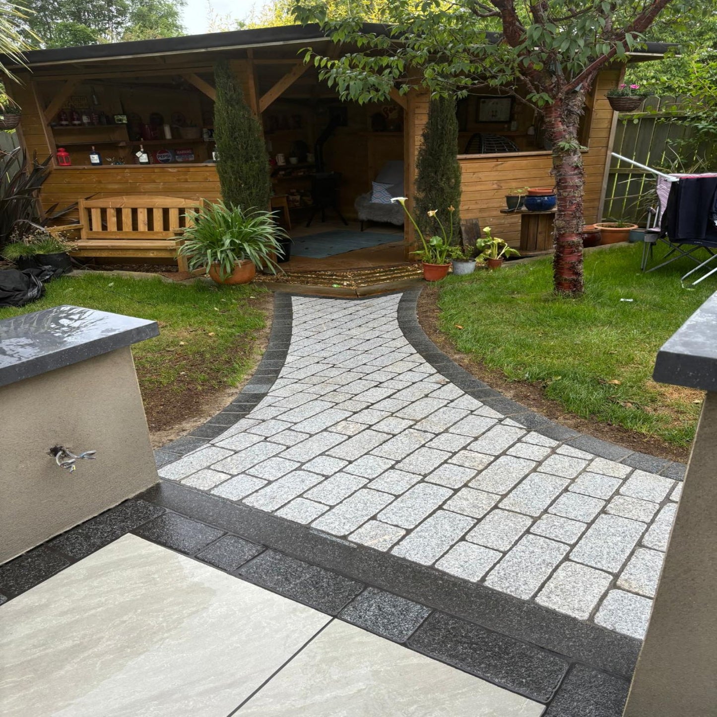 Pathway featuring Coachman's Silver Granite Paving Setts leading towards a wooden garden room. 