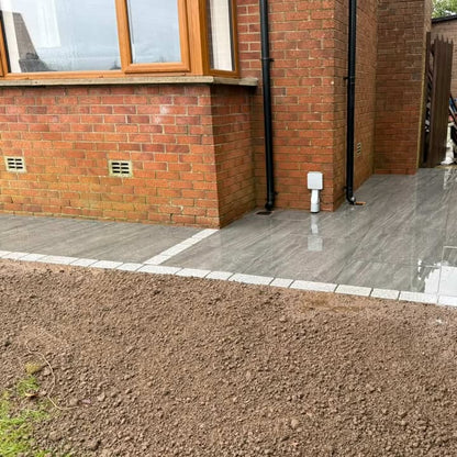 Newly installed porcelain pathway in front of a brick house. Coachman's Silver Granite Paving Setts were used to border the porcelain and gravel. 