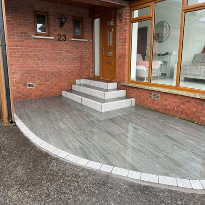 House exterior with a driveway, steps leading to the front door, and a window view of the interior. Paving bordered with Coachman's Silver Granite Paving Setts. 