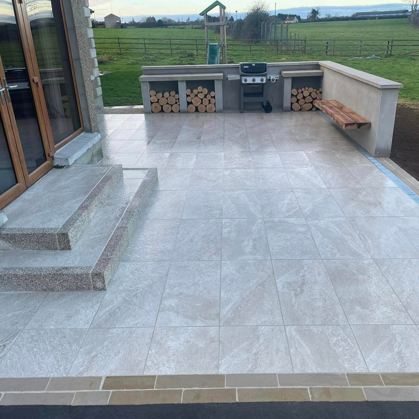 Patio area completed with Cream Twice Qz Range Porcelain Paving Tiles. BBQ and garden in the background.  