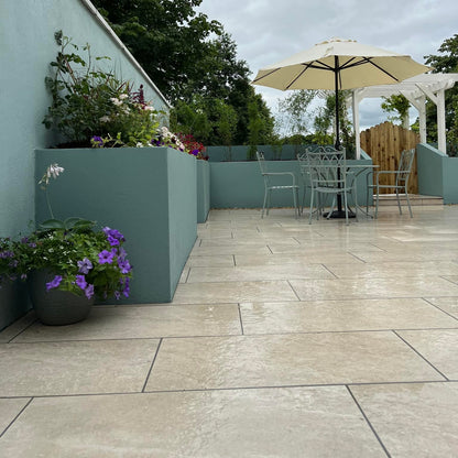 Patio area with beautiful raised blue planter walls with a table and chair garden set and large cream umbrella.  Paving is Cream Twice Qz Range Porcelain Paving Tiles. 