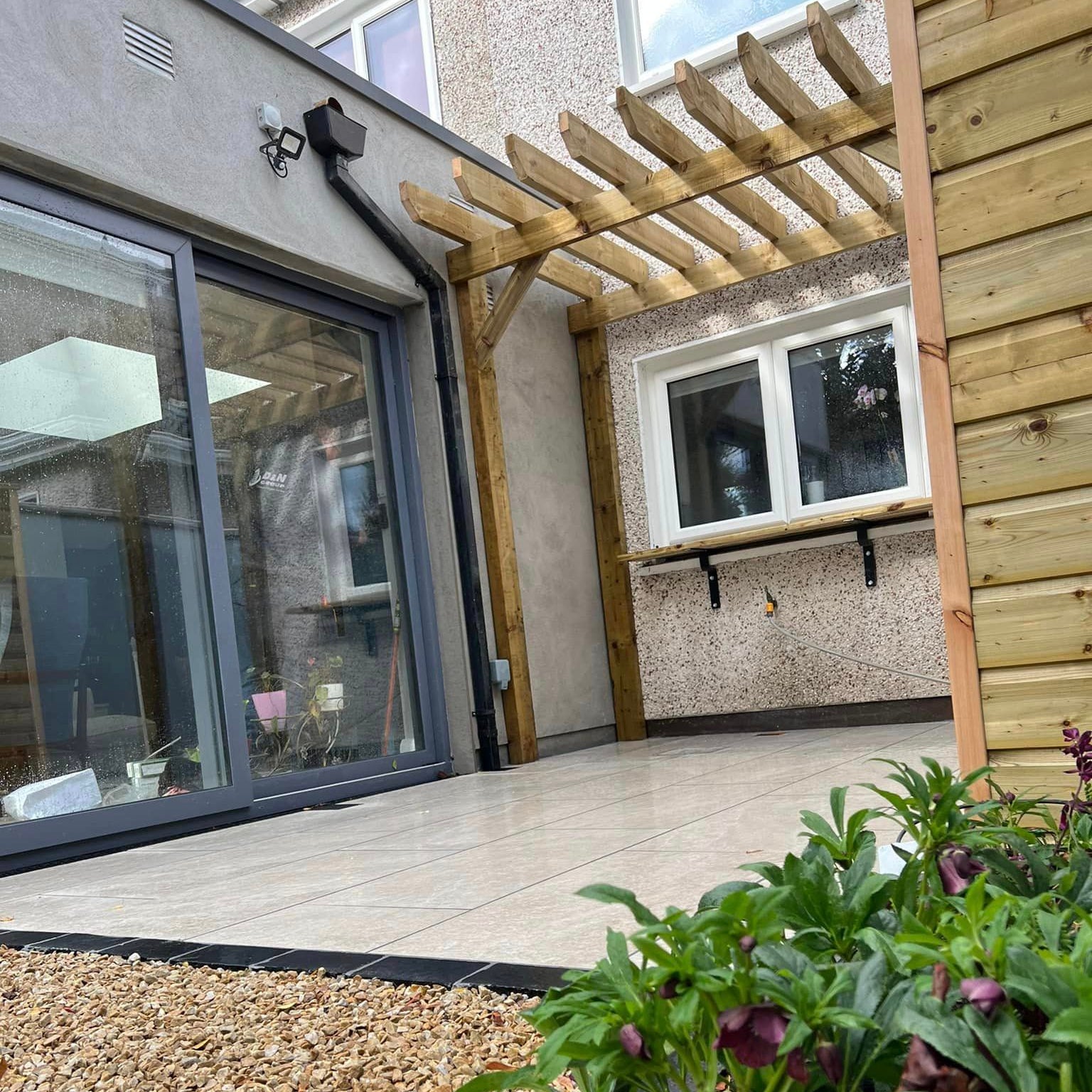 Small patio area under a wooden pergola completed using Cream Twice Qz Range Porcelain Paving Tiles. 