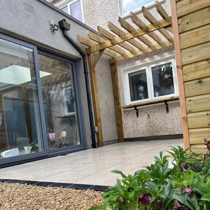 Small patio area under a wooden pergola completed using Cream Twice Qz Range Porcelain Paving Tiles. 